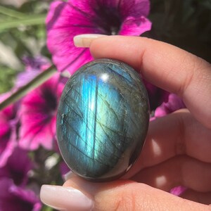 May include: A smooth, oval-shaped labradorite palm stone with iridescent blue, green, and gold hues.