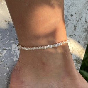 Könnte beinhalten: Ein zartes Fußkettchen aus weißen Perlen an einem Fußknöchel. Das Fußkettchen besteht aus kleinen, runden Perlen, die auf einer dünnen Kette aufgereiht sind.