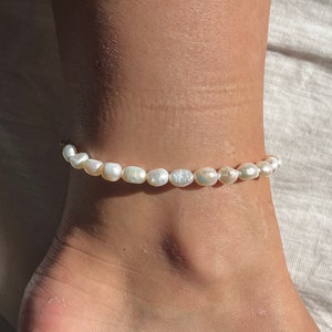 Può includere: Un braccialetto per caviglia di perle bianche con una catena delicata. Le perle sono distanziate uniformemente e hanno un leggero bagliore.