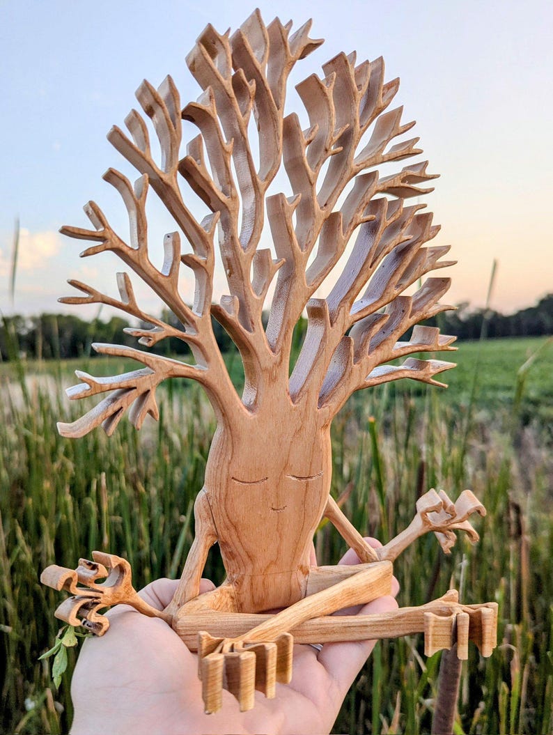 Puede incluir: Una escultura de madera de un &aacute;rbol en una pose de yoga. El &aacute;rbol tiene una cara y est&aacute; sentado con las piernas cruzadas. La escultura est&aacute; hecha de madera marr&oacute;n claro y tiene un dise&ntilde;o detallado.