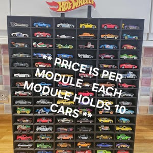 May include: Black display case with 10 rows of 10 slots for storing Hot Wheels toy cars. The case is labeled "Hot Wheels" and has the text "PRICE IS PER MODULE - EACH MODULE HOLDS 10 CARS**".