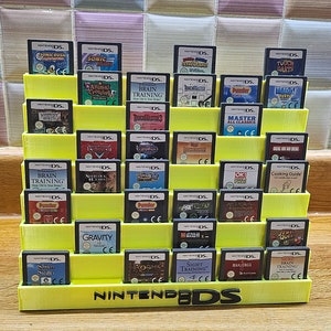 May include: A yellow plastic Nintendo DS game cartridge holder with 24 slots. The holder is filled with various Nintendo DS game cartridges. The cartridges are arranged in rows and columns. The holder has the words "Nintendo DS" printed on the front.