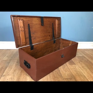 May include: A brown wooden storage chest with a hinged lid and black metal hardware. The lid is open, revealing the interior of the chest.