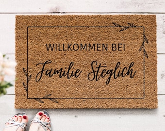May include: A brown coir doormat with the text "Willkommen bei Familie Steglich" in a black frame with a leafy design.
