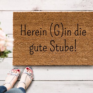 Könnte beinhalten: Eine braune Kokosmatte mit dem Text "Herein (G) in die gute Stube!" in schwarzer Schrift.