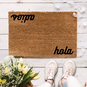 Könnte beinhalten: Eine braune Kokosmatte mit den Worten "hola" und "adios" in schwarzer Kursivschrift.