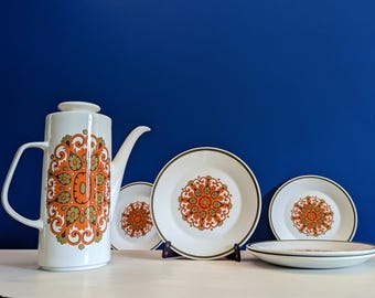 以下が含まれることがあります： オレンジと緑の花柄模様の白いセラミックコーヒーポットと、お揃いのプレート。 セットには、背の高いコーヒーポット、3つのプレート、小さなプレートが含まれています。 プレートには茶色の縁があります。