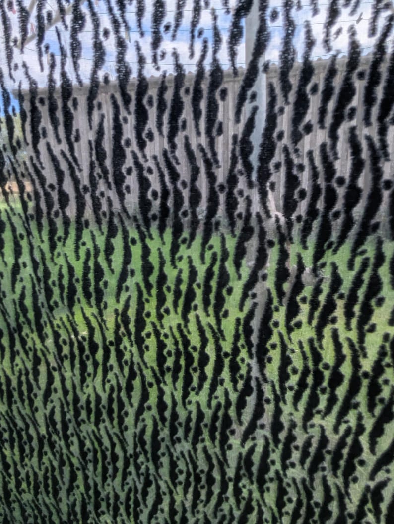 May include: A sheer fabric featuring a repeating vertical pattern of black, fuzzy, textured stripes against a translucent, light green background. The material has a distinct, raised velvet-like texture on the dark, elongated, irregular shapes.
