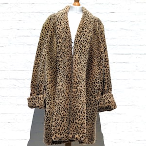 May include: A long-sleeved coat featuring a tan and brown leopard print pattern. The coat has a wide collar, a straight-cut silhouette, and folded cuffs at the end of each sleeve. The garment is displayed on a mannequin torso against a white wall.