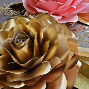 May include: Two large paper flowers, one gold and one pink, with a gold leaf design in the background.
