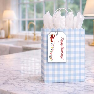 A blue and white checkered gift bag with a tag that reads "Happy Birthday!" is placed on a marble countertop in a kitchen setting.