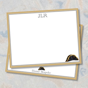 May include: Two stacked notepads with a gold border and a white interior. The top notepad has the initials "JLR" at the top and a black and gold hat graphic. The bottom notepad has the text "Honey Bespoke" and a hat graphic.