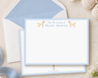 May include: A white stationery card with a light blue border, featuring two golden retriever illustrations and the text "from the nursery of BABY SMITH" in blue. The card is paired with a matching light blue lined envelope.