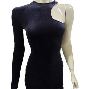May include: A black velvet one-shoulder dress with a cut-out detail on the shoulder. The dress has a fitted silhouette and a long sleeve.