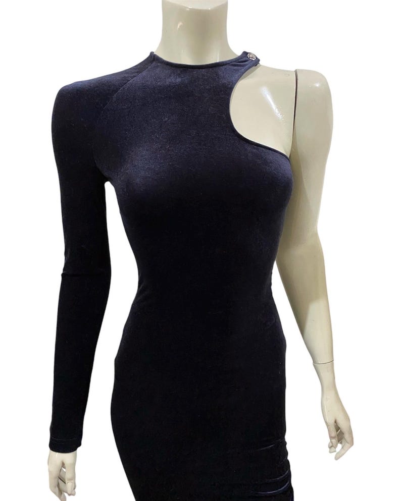 May include: A black velvet one-shoulder dress with a cut-out detail on the shoulder. The dress has a fitted silhouette and a long sleeve.