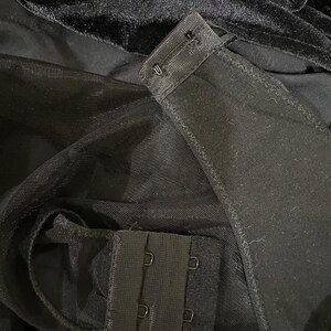 May include: Black mesh fabric with a black hook and eye closure. The fabric is folded over to show the closure.