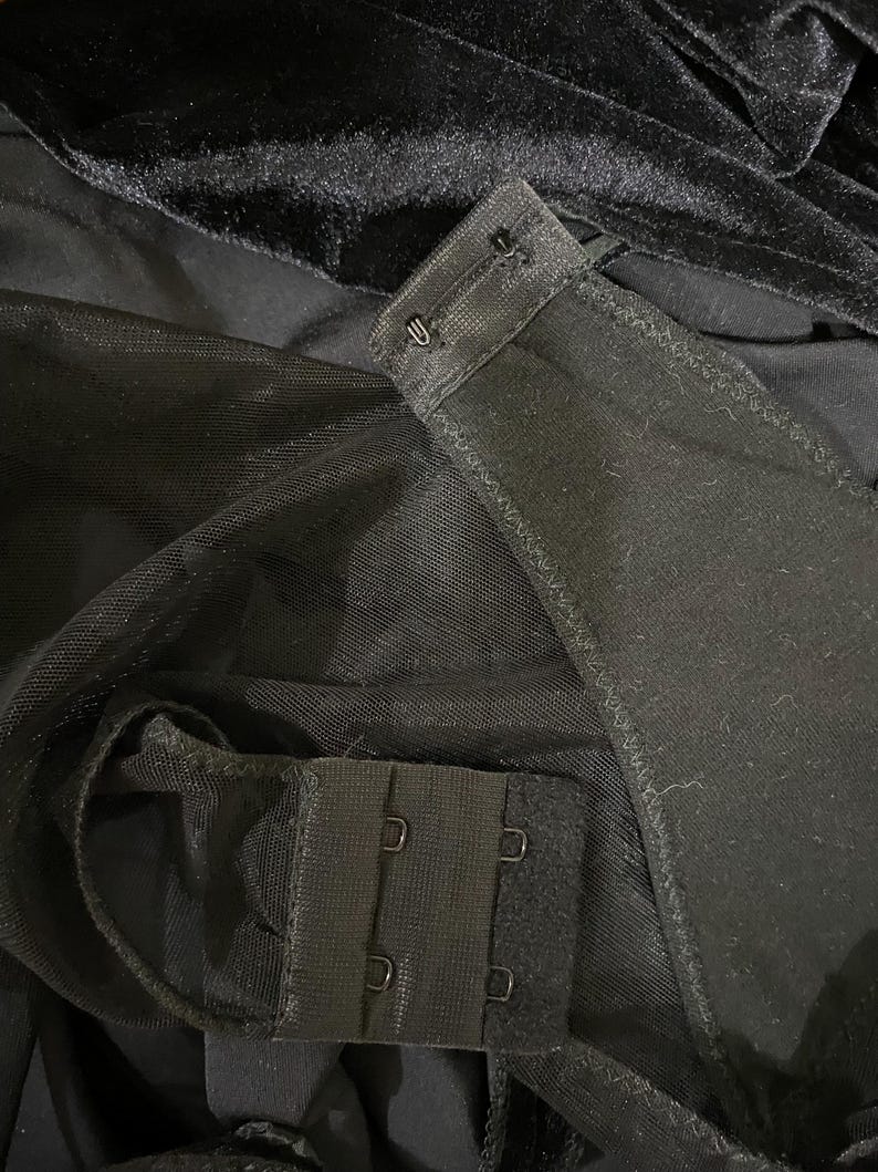 May include: Black mesh fabric with a black hook and eye closure. The fabric is folded over to show the closure.