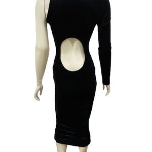 May include: A black velvet midi dress with a one-shoulder design and a cutout in the back. The dress has a fitted silhouette and a long sleeve.