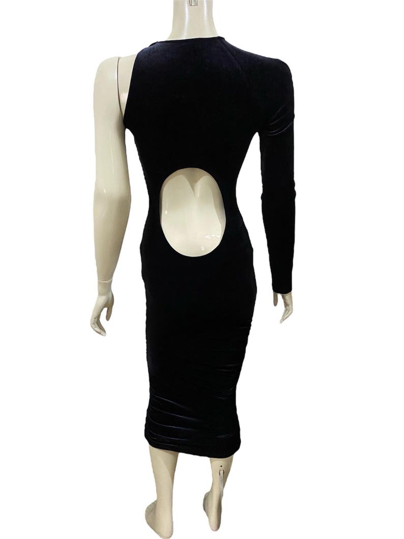 May include: A black velvet midi dress with a one-shoulder design and a cutout in the back. The dress has a fitted silhouette and a long sleeve.