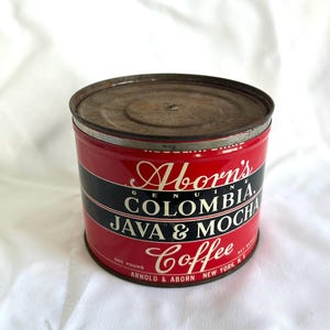 May include: Vintage Aborn's Genuine Colombia Java & Mocha Coffee tin. The cylindrical tin features a red background with a black stripe and white lettering. The tin is marked "One Pound" and "Arnold & Aborn New York, NY."