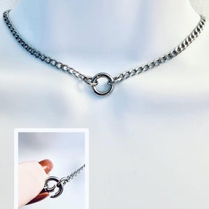 May include: Silver-toned chain choker necklace with a circular pendant. The necklace features a curb chain design and a small, round pendant in the center. The necklace is displayed on a white mannequin.