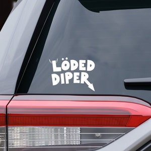 May include: A white vinyl sticker with the text "LÖDED DIPER" and an arrow pointing to the right, applied to the rear window of a silver SUV.