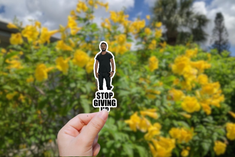 May include: A sticker featuring a man in a black shirt and jeans with the text "STOP GIVING UP" in black letters.