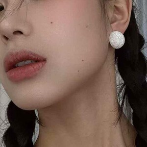 May include: A close-up of a person's face with a silver textured round earring in their right ear.