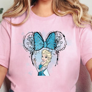 K&ouml;nnte beinhalten: Pinkes T-Shirt mit einer blauen und wei&szlig;en Schleife und einem Cartoon-Bild von Elsa aus Frozen. Die Schleife hat die Form von Mickey-Maus-Ohren.
