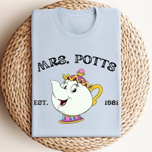 May include: Light blue t-shirt with a cartoon image of Mrs. Potts from Disney's Beauty and the Beast. The text "Mrs. Potts Est. 1981" is printed on the shirt.