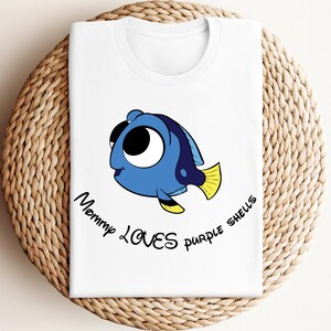 May include: White t-shirt with a cartoon blue fish with big eyes and the text "Mommy Loves Purple Shells"