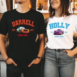 May include: Black t-shirt with the name "DARRELL" in orange arched text above a cartoon car graphic and the text "EST. 1977 DISNEY CARS". White t-shirt with the name "HOLLY" in blue arched text above a cartoon car graphic and the text "EST. 2011 DISNEY CARS".