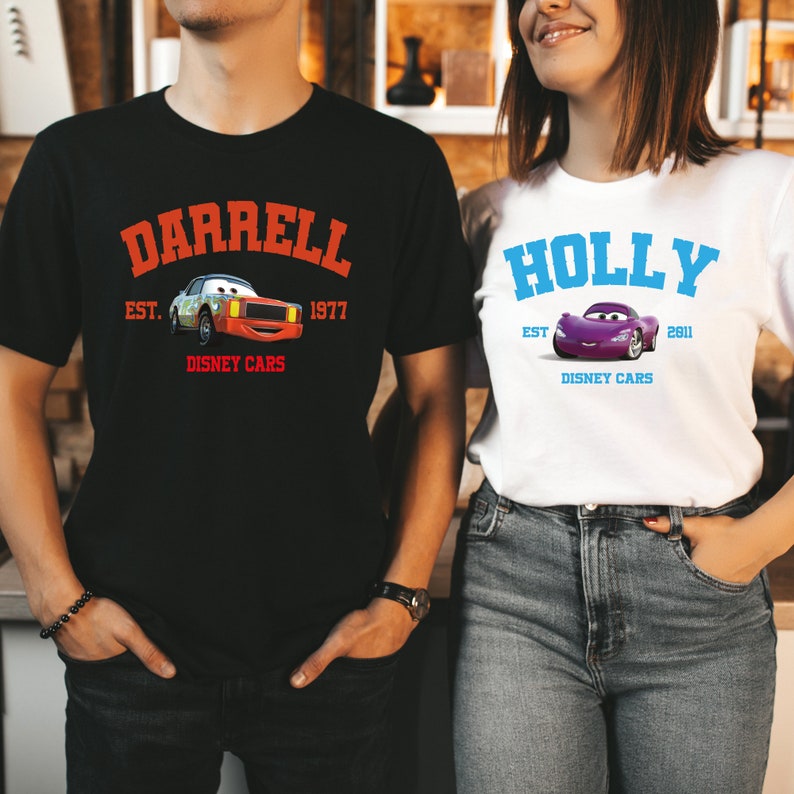 May include: Black t-shirt with the name "DARRELL" in orange arched text above a cartoon car graphic and the text "EST. 1977 DISNEY CARS". White t-shirt with the name "HOLLY" in blue arched text above a cartoon car graphic and the text "EST. 2011 DISNEY CARS".