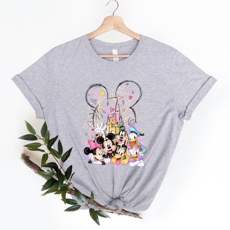 May include: A gray t-shirt with a colorful illustration of Mickey Mouse, Minnie Mouse, Donald Duck, Goofy, and Pluto in front of a pink castle. The illustration is surrounded by hearts and stars.