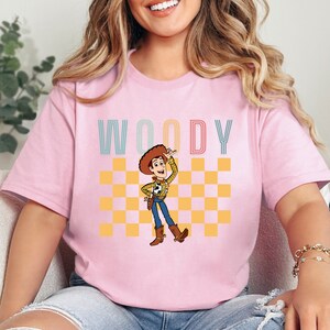 a woman sitting on a couch wearing a pink woody t - shirt