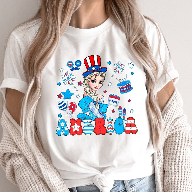 May include: White t-shirt with a cartoon image of a girl wearing a red, white, and blue hat and holding a cup that says "4 JULY". The word "AMERICA" is written in red, white, and blue letters with stars and fireworks around the girl.