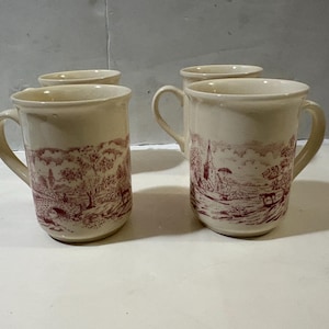 Può includere: Quattro tazze in ceramica color crema con un disegno a paesaggio rosso. Le tazze hanno un manico e una forma cilindrica. Il disegno del paesaggio presenta alberi, edifici e un ponte. Adatto per caffè o tè.