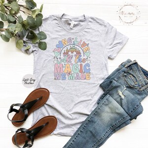 May include: A light gray heather t-shirt with a colorful graphic design featuring a castle, Mickey Mouse ears, and the text "Long Live All the Magic We Made".