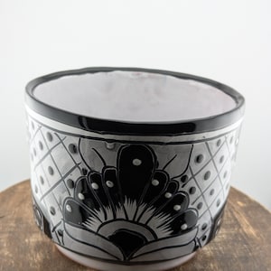 May include: Black and white ceramic planter with a floral design. The planter has a black rim and a white background with black floral details.