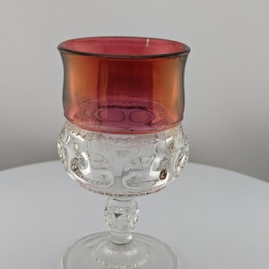 May include: A clear glass goblet with a red, iridescent top. The goblet has a round, textured bowl and a stem with a round base.