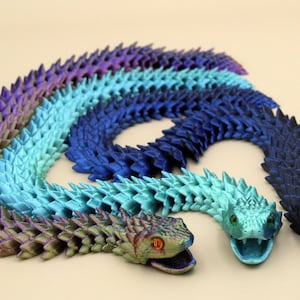 May include: Three articulated snake toys in shades of purple, blue, and teal. Each snake has a detailed, textured surface and open mouths. The snakes are arranged in a circular pattern.