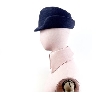 side view of the navy felt hat on a mannequin, with focus on a sculptural navy blue field hat
