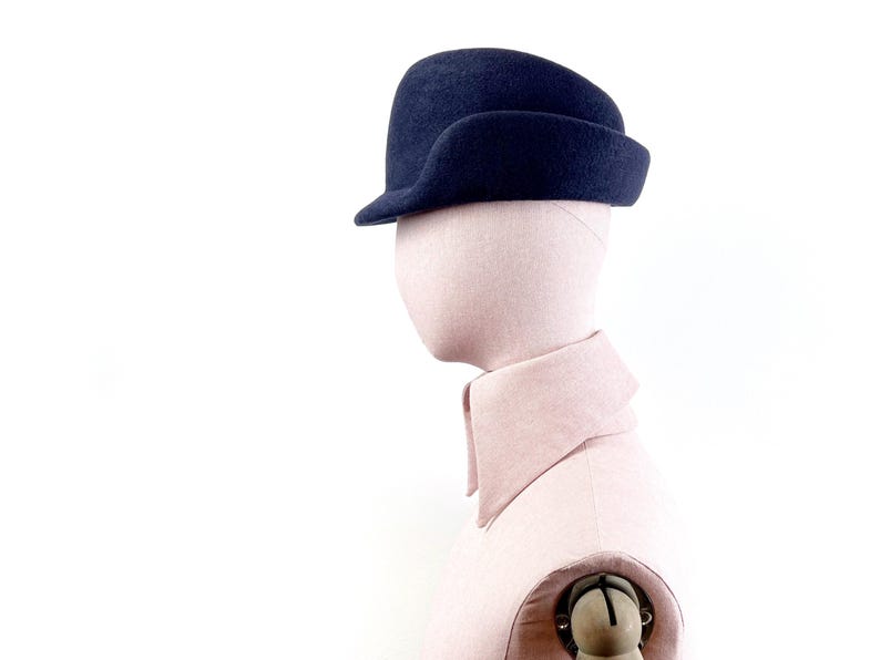 side view of the navy felt hat on a mannequin, with focus on a sculptural navy blue field hat
