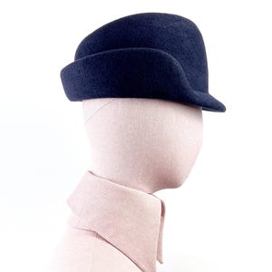 side view of a navy sculptural felt hat on a mannequin, showing the right profile with curved mocked ear flap and short brim.