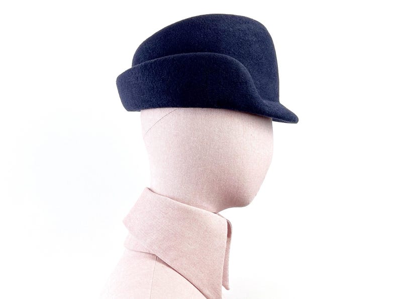 side view of a navy sculptural felt hat on a mannequin, showing the right profile with curved mocked ear flap and short brim.