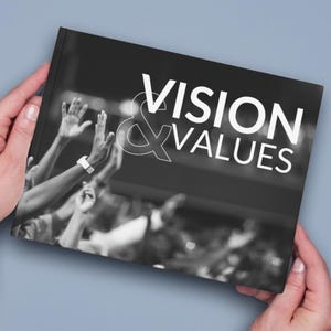 May include: Black and white photo of a crowd of people with their hands raised in the air. The text "VISION & VALUES" is printed in white on a black background.