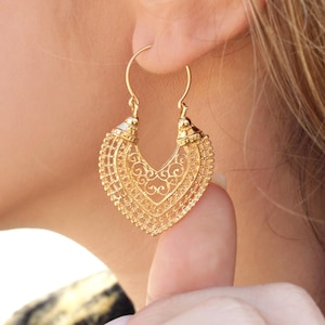May include: Gold filigree earrings with a heart-shaped design. The earrings are dangling and have a delicate, intricate pattern.