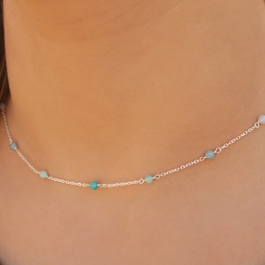 Pode incluir: Um delicado colar de corrente de prata com pequenas pedras turquesa e azuis.