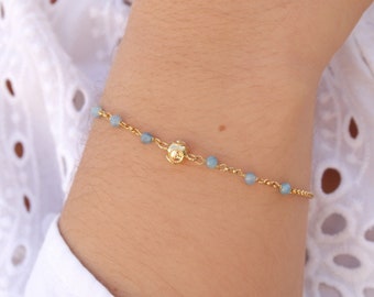 May include: A delicate gold chain bracelet with small light blue beads and a gold charm.