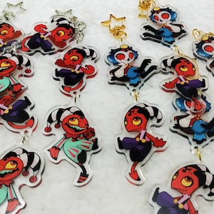 Puede incluir: Un conjunto de 12 abalorios acrílicos coloridos con personajes de dibujos animados con detalles rojos, azules y verdes. Los abalorios están unidos a cadenas doradas con abalorios en forma de estrella.